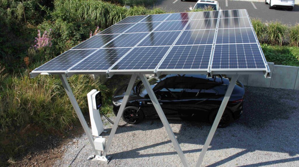 Referenz-Foto eines ENnergy Solarcarports - Doppelcarport mit Photovoltaikmodulen auf dem Dach, ein E-Auto steht unter dem Carport und wird von der ENnergy Ladestation aufgeladen
